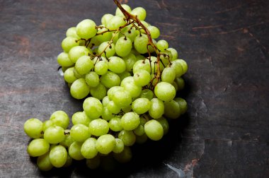 Olgun yeşil üzümlü ve su damlalı bir dal. Tahta arka planda sulu üzümler, yakın plan. Fotokopi alanı olan koyu mutfak masasında üzümler