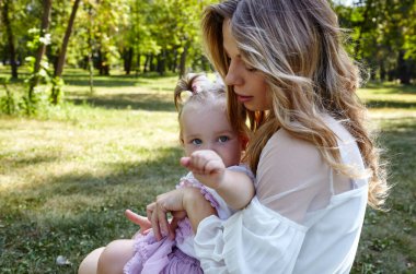 Anne ve kızı yazın şehir parkında yürürler. Çocukluk, eğlence ve insan konsepti - mutlu aile doğada dinlenir ve iyi vakit geçirir.