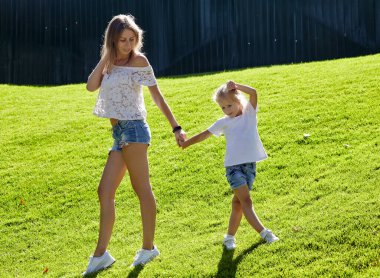 Anne ve kızı yaz parkında çimlerde yürüyor. Çocukluk, eğlence ve insan konsepti. Mutlu aile istirahatı ve iyi vakit geçirmek.