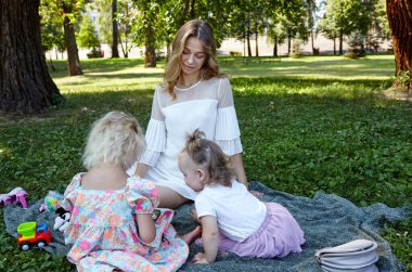 Anne ve kızları yaz parkında ekose üzerinde oturuyorlar. Çocukluk, eğlence ve insan konsepti. Mutlu aile istirahatı ve iyi vakit geçirmek.