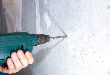Man is drilling hole in the concrete wall. Repair works. Maintenance in the apartment. clipart