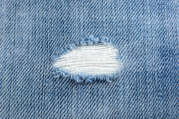 Ripped blue hipster jeans material. Destroyed denim Cloth texture. Close up.