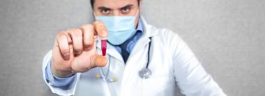 Laptop 'ın yanında kapalı alanda maske takan bir doktor. Koronavirüs salgını sırasında mesafeli tedavi. Pratisyen hekimin elinde kanla dolu bir şişe var. Virüs analizde. Çevrim içi danışmanlık.