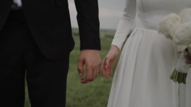Damat ve gelin el ele tutuşuyor. Mutlu evlilik videoları. Romantik bir ilişki. Beyaz elbise. Yaklaşın, ağır çekim..