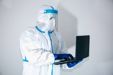 Doktor koruyucu giysi, gözlük, maske ve eldiven takıp dizüstü bilgisayarda çalışıyor. Virüs salgını koruyucuları. Coronavirus (COVID-19). Sağlık hizmetleri kavramı.