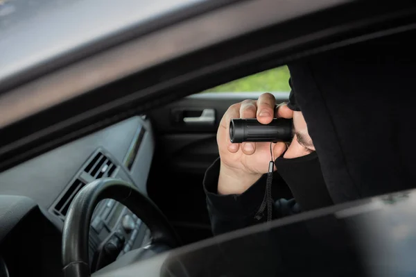 Spying from the car. Man with binoculars in black clothes. Criminal concept. Detective work.