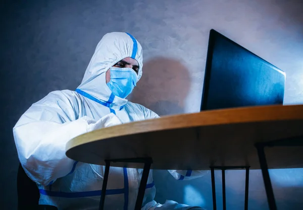 Doctor wearing medical protective suit, medical mask and gloves working on laptop. Protection mers by virus epidemic. Coronavirus (COVID-19). Healthcare concept.