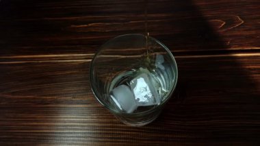 Barmen içki koyuyor. Bardağa dökülen viskinin ahşap masadaki buz küpleriyle en üst görüntüsü. Kapat..