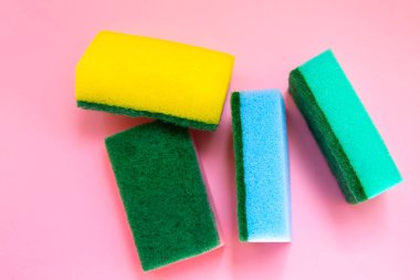 Pembe arka planda bulaşık yıkamak için renkli süngerler. Yapay lif çevre dostu bir alet değil. Mutfak eşyaları..