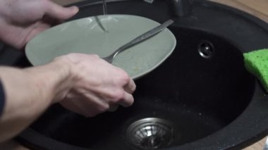 Erkek elleri mutfak lavabosunda tabağı durular. Bulaşık yıkama rutini, yakın çekim, 4K video. Yumuşak odaklı.