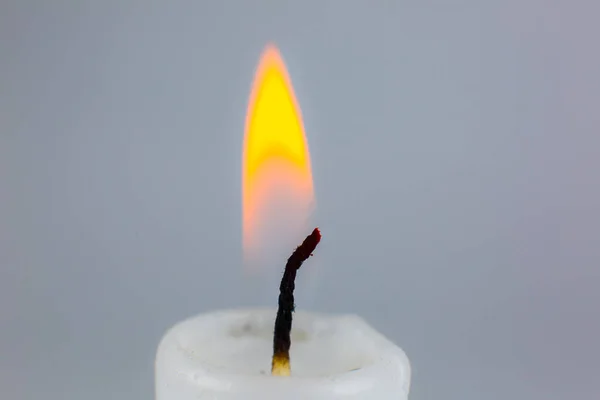 Burning white candle on the gray background. Close up photo.