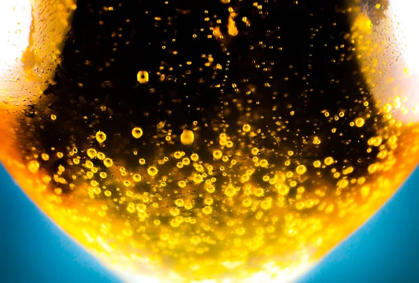 Liquid gold-yellow gasoline bubbles background on beer or champagne glass. Close up, macro shot. Soft focus photo.