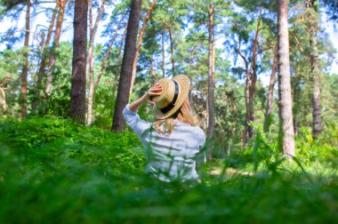 Hasır şapkalı hippi kız ormanda oturuyor. Seyahat tutkusu konsepti. Seyahat fikirleri. Doğada, çimlerin üzerinde güzel bir kadın. Yaz titreşimleri.