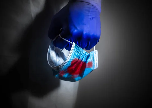 Doctor in medical protective suit and gloves, holding medical mask in blood in his hand. The end of virus pandemic. Protection mers by virus epidemic. Coronavirus (COVID-19). Healthcare concept.