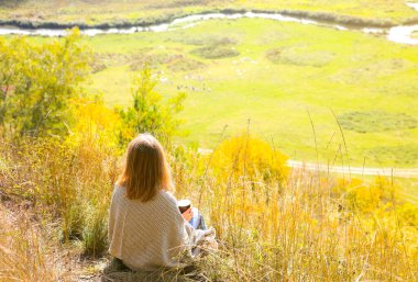 Sonbahar doğasında kahve içen güzel bir kız. Dağlarda bir bardak sıcak içecek. Keyifli bir ortam. Kırmızı ve sarı yapraklar. Karantina süresince kendini izole et. Hayatı düşün..