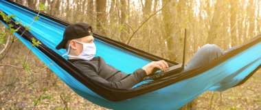 Maskeli adam hamakta dizüstü bilgisayarla çalışıyor. Doğadaki karantina sırasında serbest çalışan biri. Corona virüsü yüzünden uzak çalışma. İşsizlik sorunu olan insanlar. Arama çalışması. Covid-19 dönemi. Kişisel tecrit.