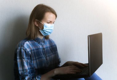 Tıbbi maskeli kadın evde çalışıyor. Karantina zamanında online serbest çalışmalar. Laptop ellerde. Coronavirüs pandemisi. Ekonomik kriz alternatifleri.