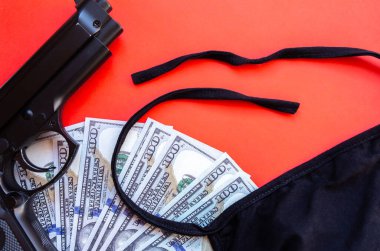 Silah, dolar parası ve kırmızı arka planda koruyucu tıbbi maske. Ekonomik kriz, soygun, işsizlik kavramı. Koronavirüs hastalarının karantina sırasındaki izolasyonları.