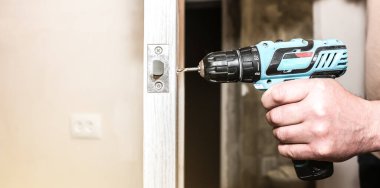 Adam matkapla kapı kolunu kuruyor. Onarım işe yarıyor. Dairede bakım var..