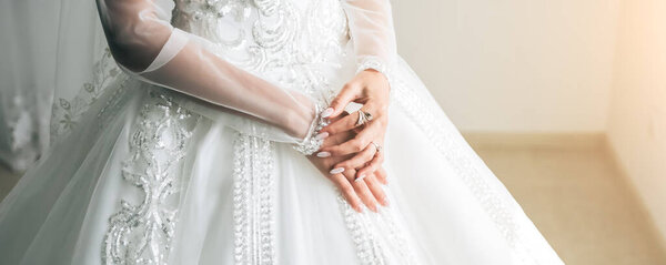 Bride is holding hands with golden rings on her luxury long sleeve dress. Beautiful nails. Artificial crystal diamonds. Wedding jewellery.