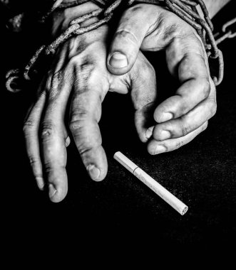 Adamın elleri sigaranın yanında paslı zincirlerde. Sigara bağımlısı. Tehlikeli bir alışkanlık..