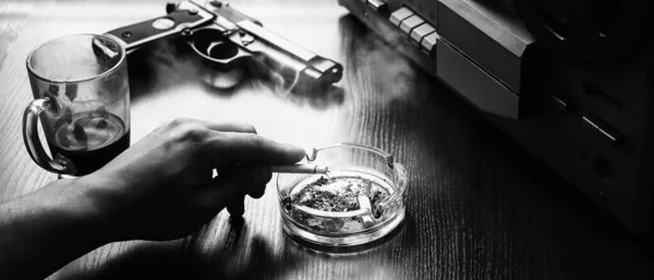 Special agent listens on the reel tape recorder. Officer is smoking a cigarette. KGB spying on conversations. Hand with cigarette near the ashtray. Gun on the table.