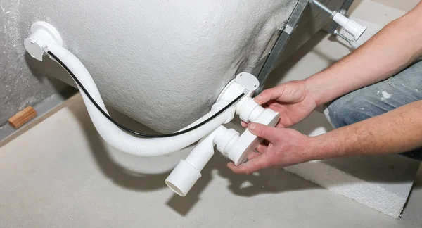 Banyo kurulumu. İşçi hortum borusuyla drenaj yapıyor. Dairede bakım onarımı var. Yenileme işlemi.