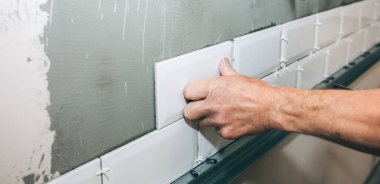 Adam gri betona beyaz fayanslar koyuyor. Bakım onarımı dairede tadilat yapıyor. Kapalı alanda restorasyon. İşlem devam ediyor.