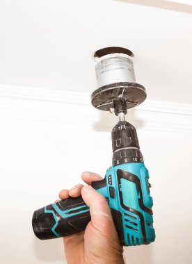 Adam elinde elektrikli matkap tutuyor. Tavanda büyük bir delik var. Bakım onarımı dairede işe yarıyor. İçerideki restorasyon.