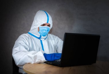 Tıbbi koruyucu giysi giyen doktor, tıbbi maske ve eldivenler laptopta çalışıyor. Virüs salgını koruyucuları. Coronavirus (COVID-19). Sağlık sigortası konsepti. Bir salgın covid içinde uzaktan çalışma.