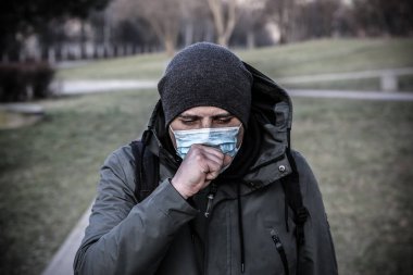 Coronavirüs salgını. Maskeli bir adam dışarıda öksürüyor. Tehlikeli grip vakaları. Salgın hastalık. Sağlık sorunu kavramı.