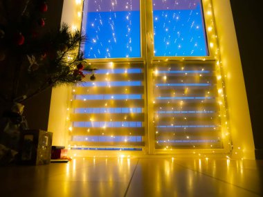 Güzel, bulanık, yanıp sönen sarı ışık. Penceresinde çelenkler olan bir ev dekorasyonu, gece aydınlatması. Neşeli arkaplan.