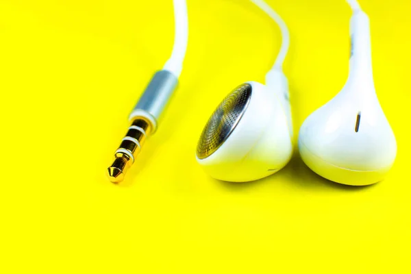 White Earphones lying on the yellow background. Modern music concept. Audio technology. Close up photo.