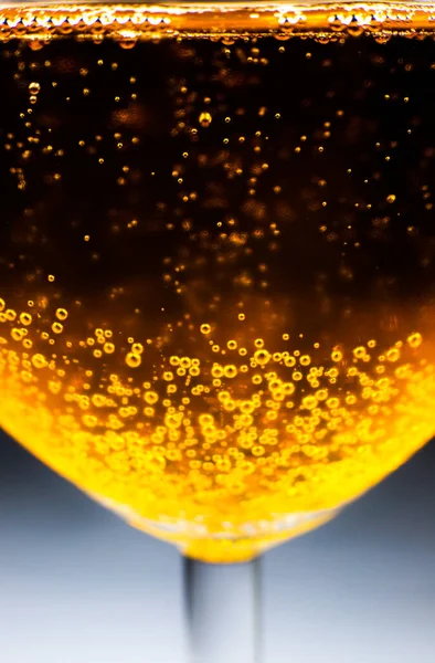 Blurred Liquid gold-yellow gasoline bubbles background on beer or champagne glass. Close up, macro shot. Soft focus photo.