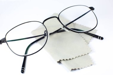 Siyah çerçeveli gözlük ve beyaz arka planda gözlük temizleme bezi. Fotoğrafı kapat..