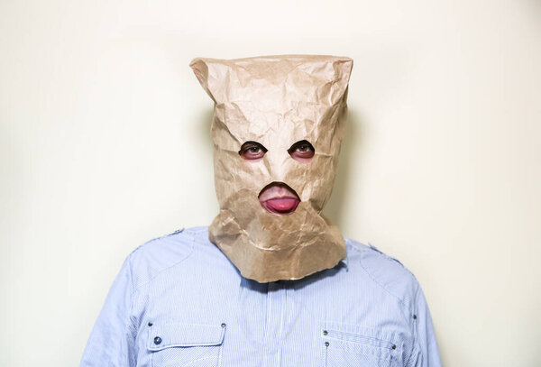 Kraft paper bag is on the man's head. Holes for eyes. Funny idea. Guy is showing his tongue.