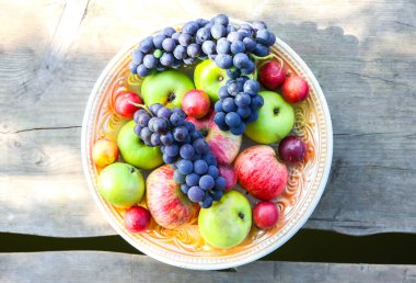 Tahta köprüde meyveli tabak. Kırsal yaz meyveleri düzlüktü. Sağlıklı vejetaryen yaşam tarzı konsepti. Yaz titreşimleri. Nehir kenarında piknik.