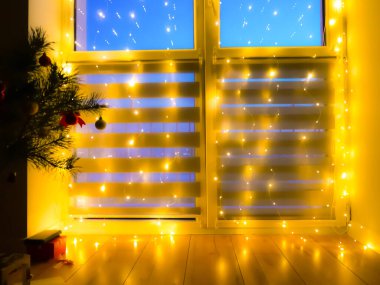 Güzel, bulanık, yanıp sönen sarı ışık. Penceresinde çelenkler olan bir ev dekorasyonu, gece aydınlatması. Neşeli arkaplan.