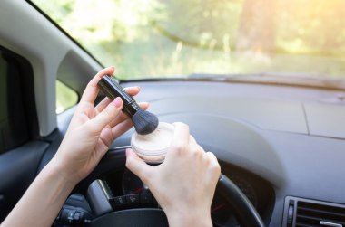 Kadın, arabada makyaj yapıyor. Direksiyonda yüz pudrası olan kız. Yolda tehlikeli bir durum var. Kaza olasılığı var..