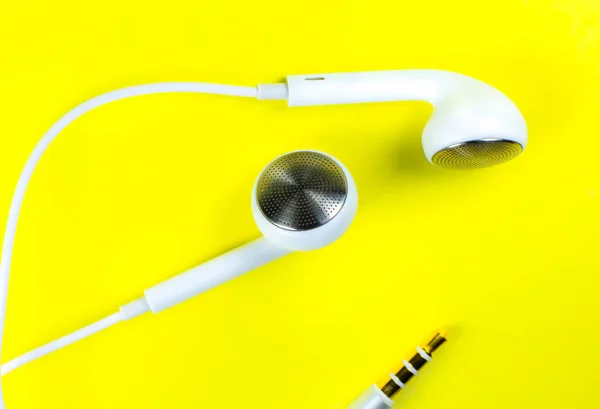 White Earphones lying on the yellow background. Modern music concept. Audio technology. Close up photo.