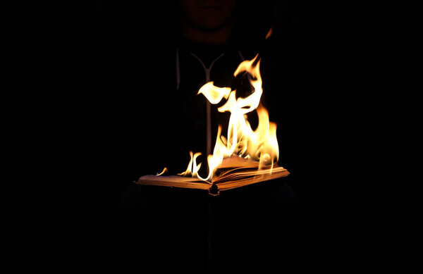 Man is holding burning book on fire at night. People don't like reading. Intellectual problems.
