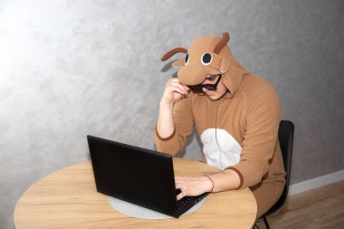 İnek kostümü giymiş bir ofis çalışanı. Laptopun yanında komik hayvan pijamalı adam. Adam evden çalışıyor. Arama işi, işsizlik konsepti, ekonomik kriz. Uzak çalışma.