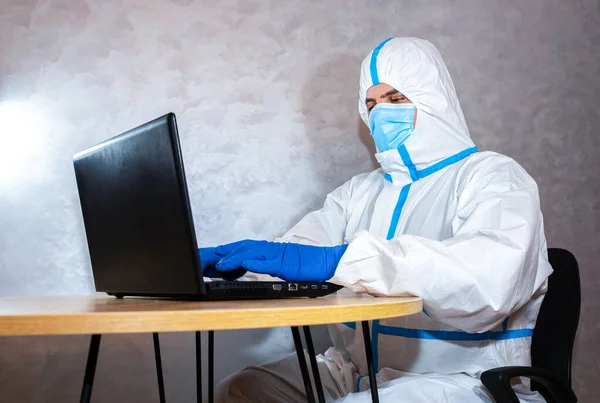 Doctor wearing medical protective suit, medical mask and gloves working on laptop. Protection mers by virus epidemic. Coronavirus (COVID-19). Healthcare concept. Remote work in a pandemic covid.
