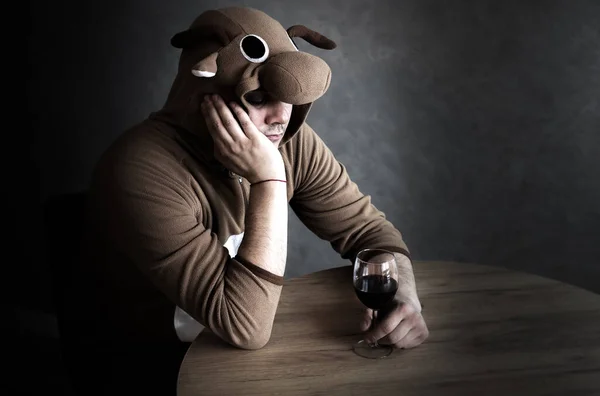 Office worker in cosplay costume of a cow. Guy in the funny animal pyjamas near the a glass of wine. Alcoholic addict, Lost job, unemployment concept, economic crisis. Depression and alcoholism.