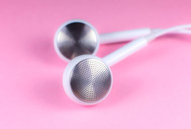 Pembe arka planda beyaz kulaklıklar var. Modern müzik konsepti. Ses teknolojisi. Fotoğrafı kapat..