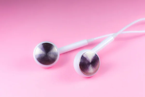 White Earphones lying on the pink background. Modern music concept. Audio technology. Close up photo.