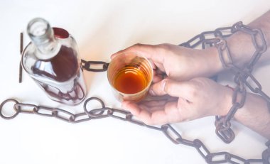 Şişenin yanındaki paslı zincirlerde bir adamın elleri. Alkole bağımlı. Tehlikeli bir alışkanlık..