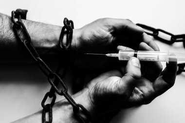 Şırınganın yanında eski paslı zincirlerde bir adamın elleri. Uyuşturucu bağımlısı. Tehlikeli bir alışkanlık..