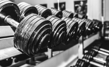Spor salonundaki çiğ dambıllar. Fitness sporu motivasyonu. Sağlıklı yaşam tarzınız kutlu olsun. Çubuk ağırlıklarıyla egzersiz. Siyah beyaz fotoğraf.