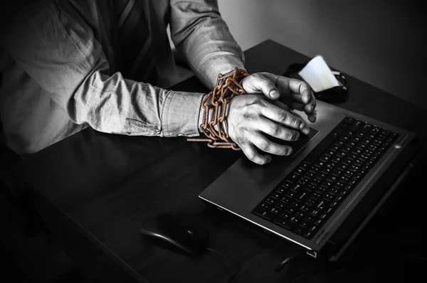 Man\'s hands in old rusty chains. In the trap of office work. Routine job. Manager near the laptop.
